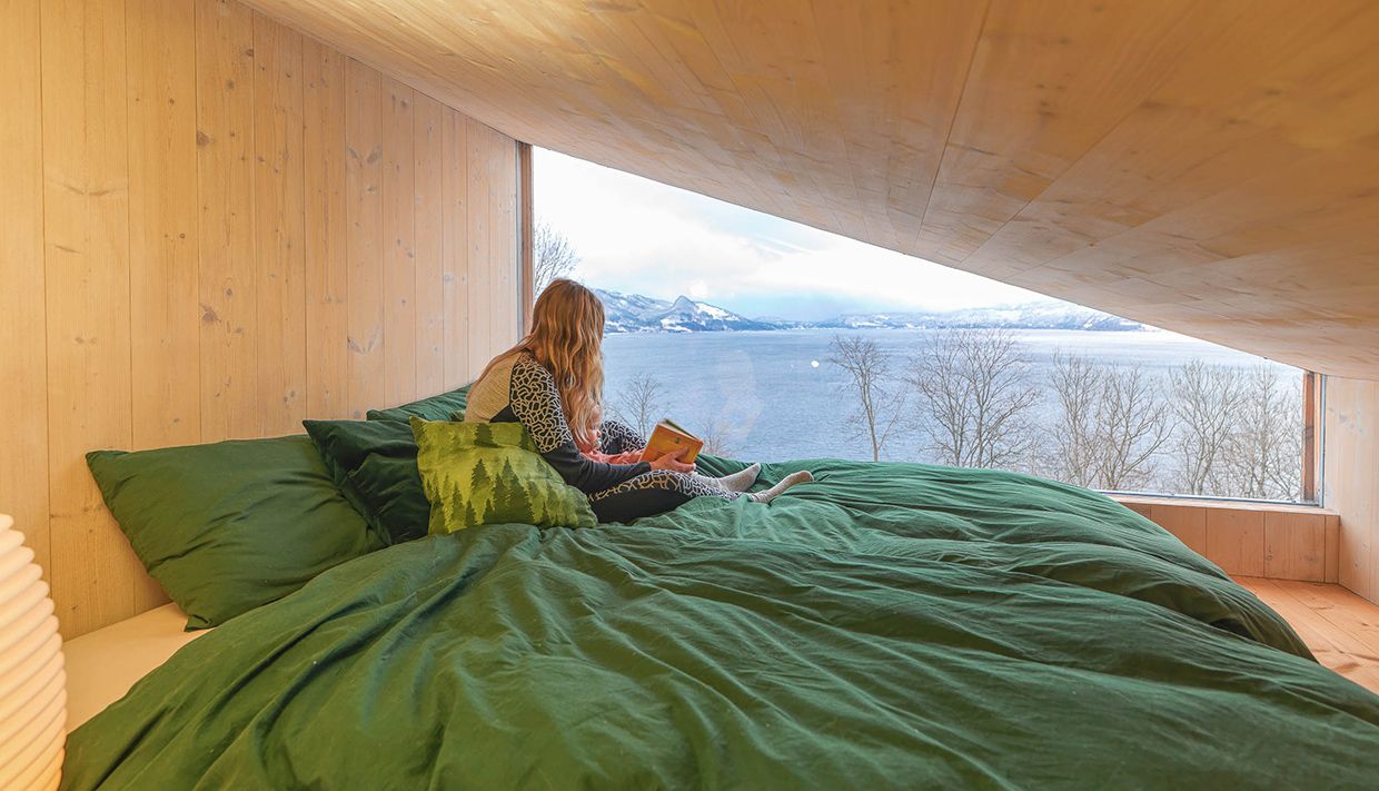 Guest relaxing in bed with fjord view in the cabin near Hardangerfjord.