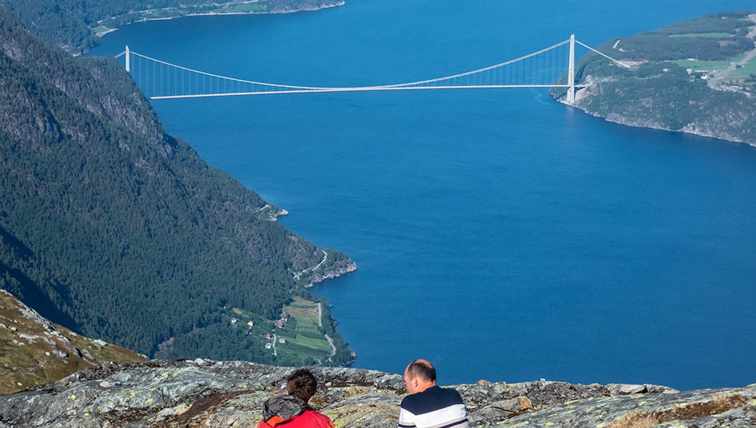 To personar kviler på fjellet med utsikt mot ei fjordbru i Hardanger.