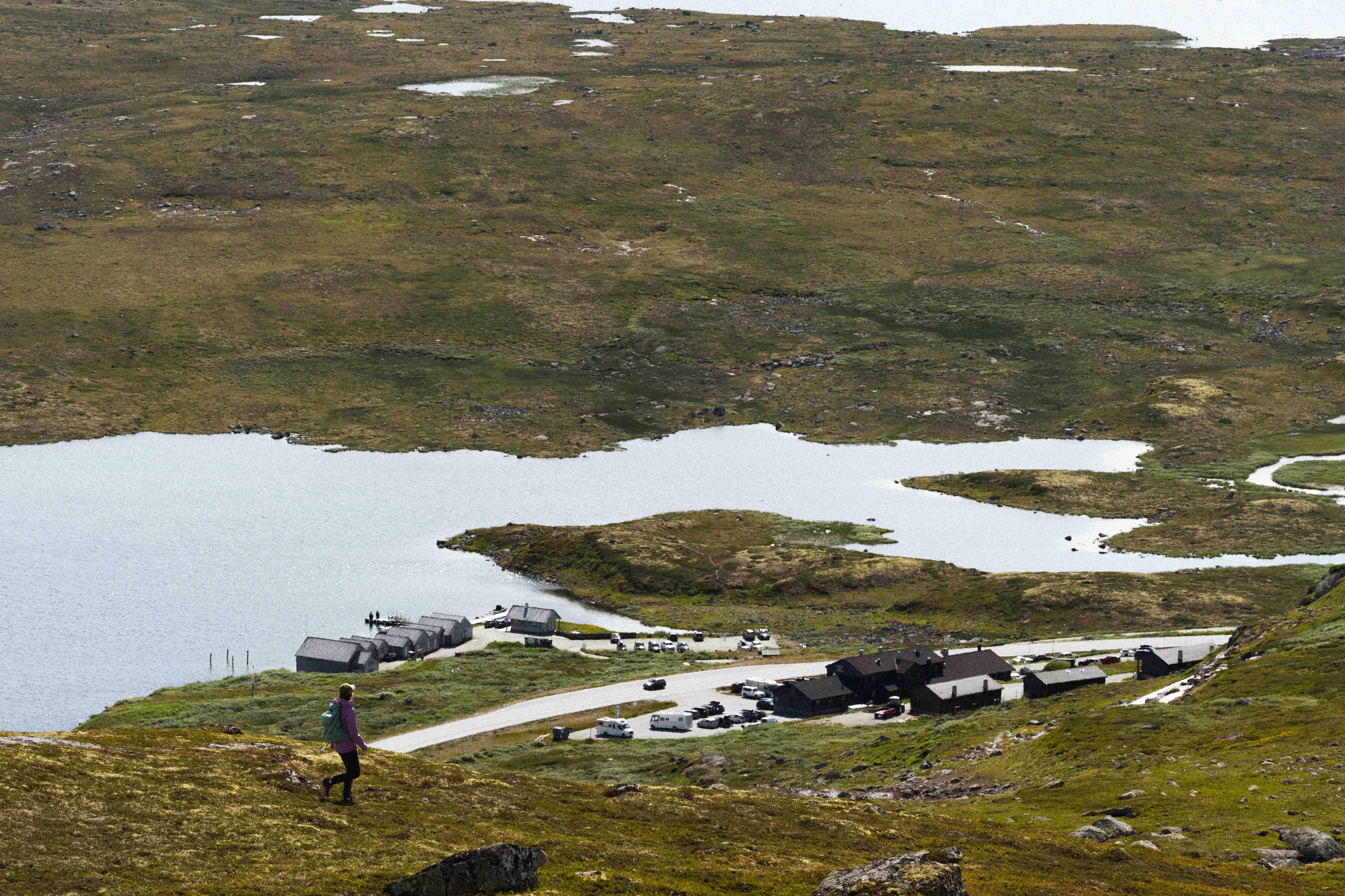 A female hiker standing on a hill, looking down at Halne Fjellstugu.