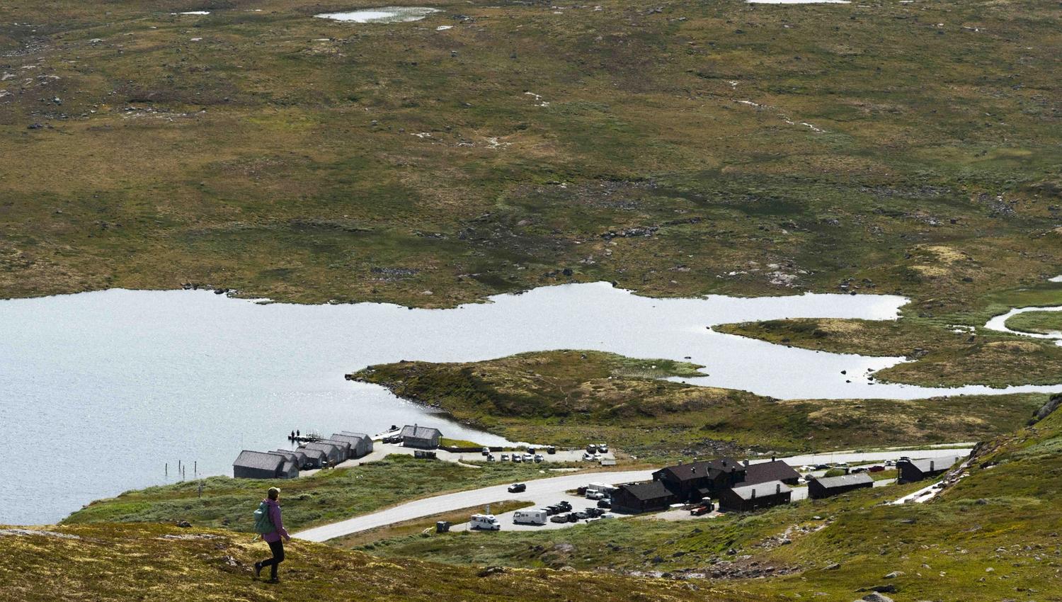 A female hiker standing on a hill, looking down at Halne Fjellstugu.