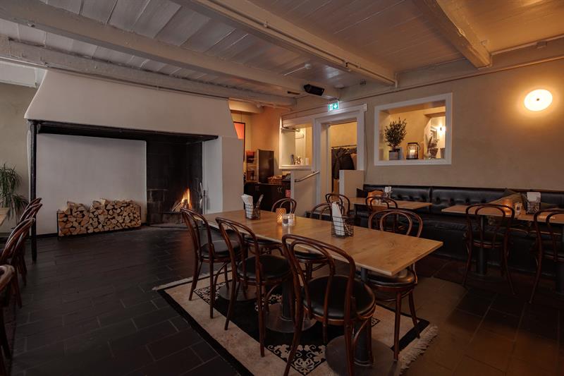 Cosy dining room with a fireplace, wooden tables and chairs creating a warm and intimate atmosphere.