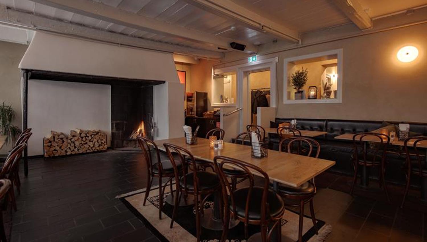 Cosy dining room with a fireplace, wooden tables and chairs creating a warm and intimate atmosphere.