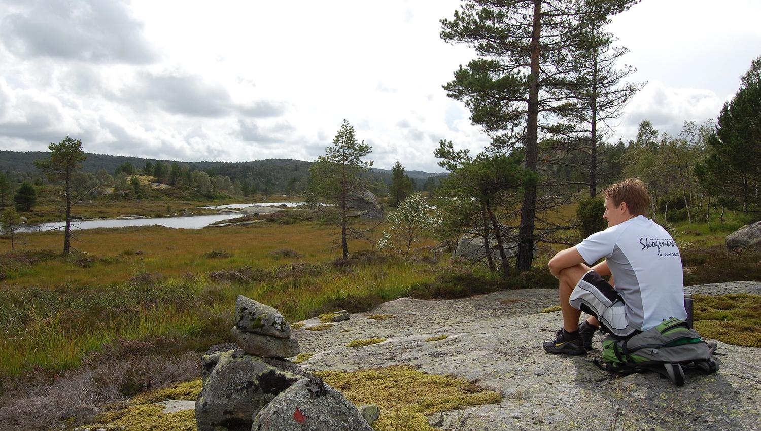 En mann som sitter på sekken sin og ser ut mot landskapet med vanndam