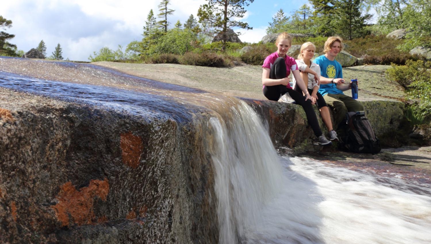 gruppe ungdom sitter ved en liten foss