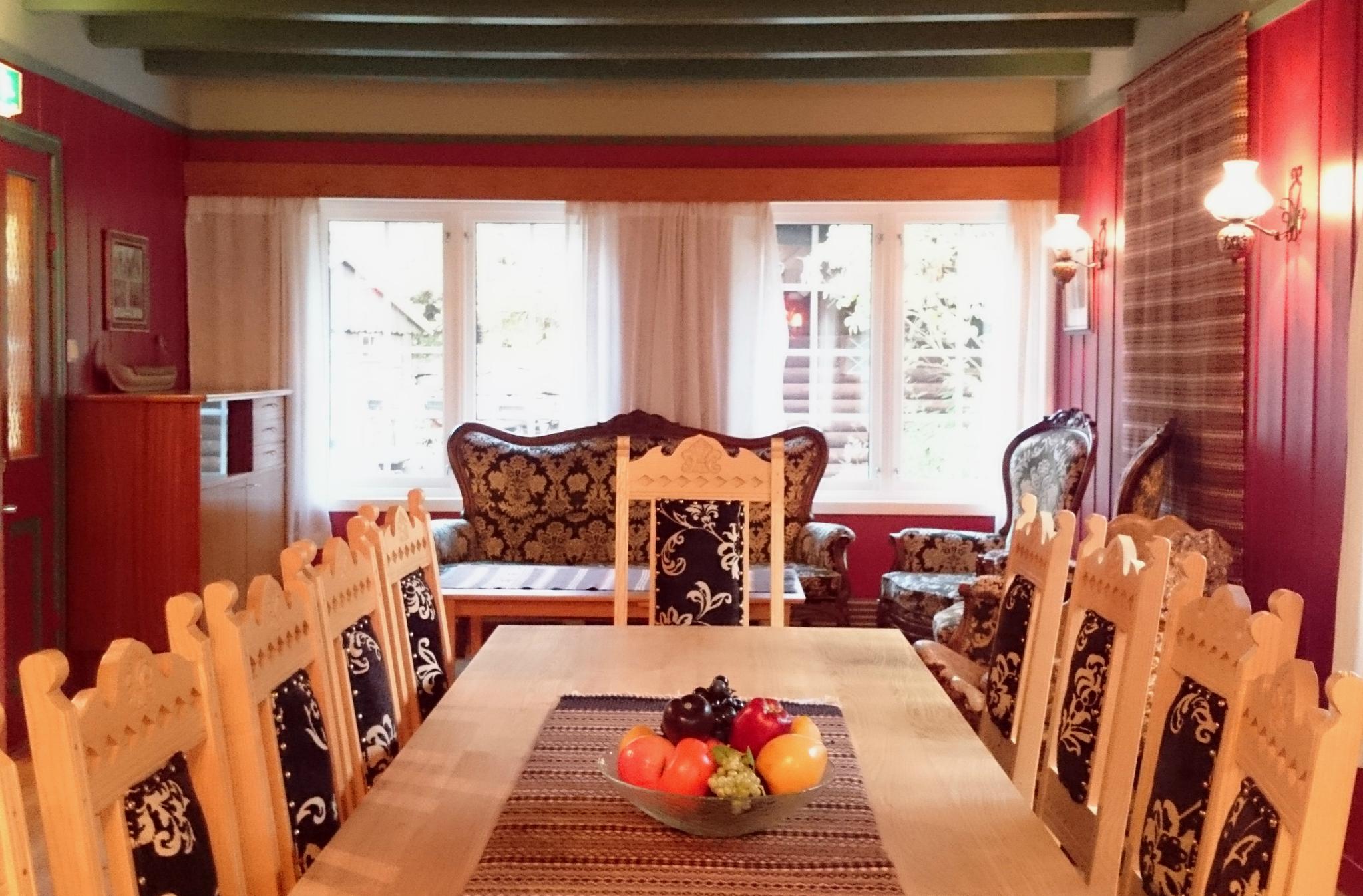 Lys og triveleg stove på Ullensvang Gjesteheim med tradisjonelle møblar, broderte detaljer og utsikt mot hagen.