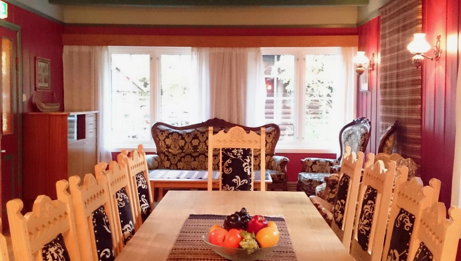 Lys og triveleg stove på Ullensvang Gjesteheim med tradisjonelle møblar, broderte detaljer og utsikt mot hagen.
