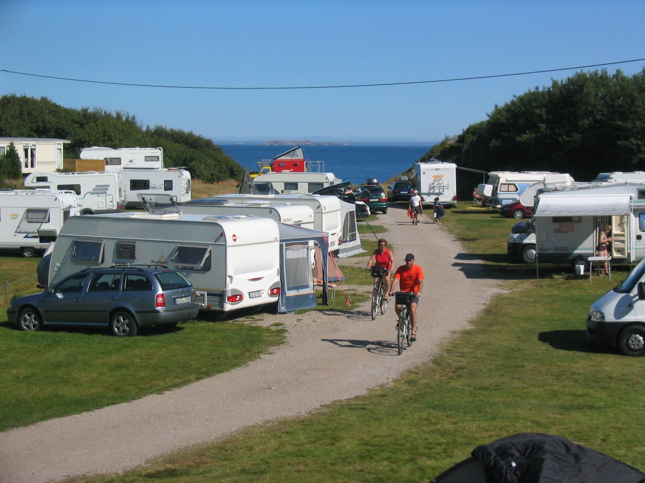 Lindesnes Camping og Hytteutleie, en sti lang mellom campingvognene. To syklister med knallrøde t-skjorter sykler på stien.