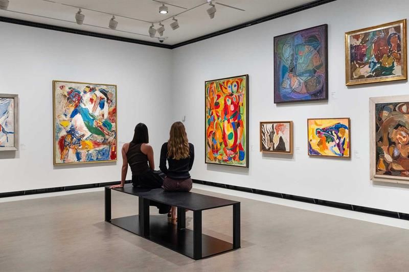 To jenter sittende på en benk som ser på malerier i et utstillingsrom