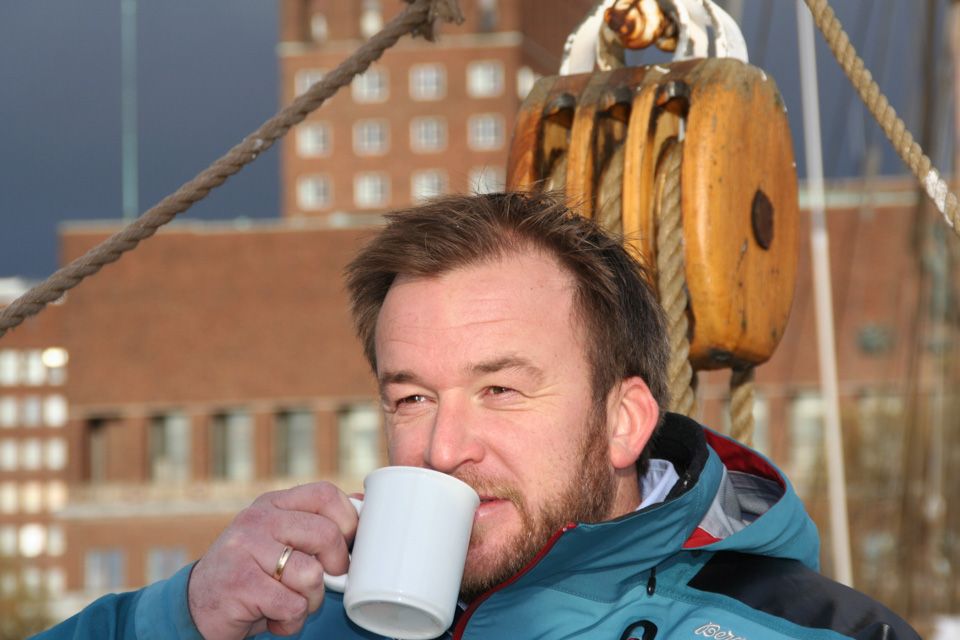 Man drinking coffee on deck with City Hall in the background