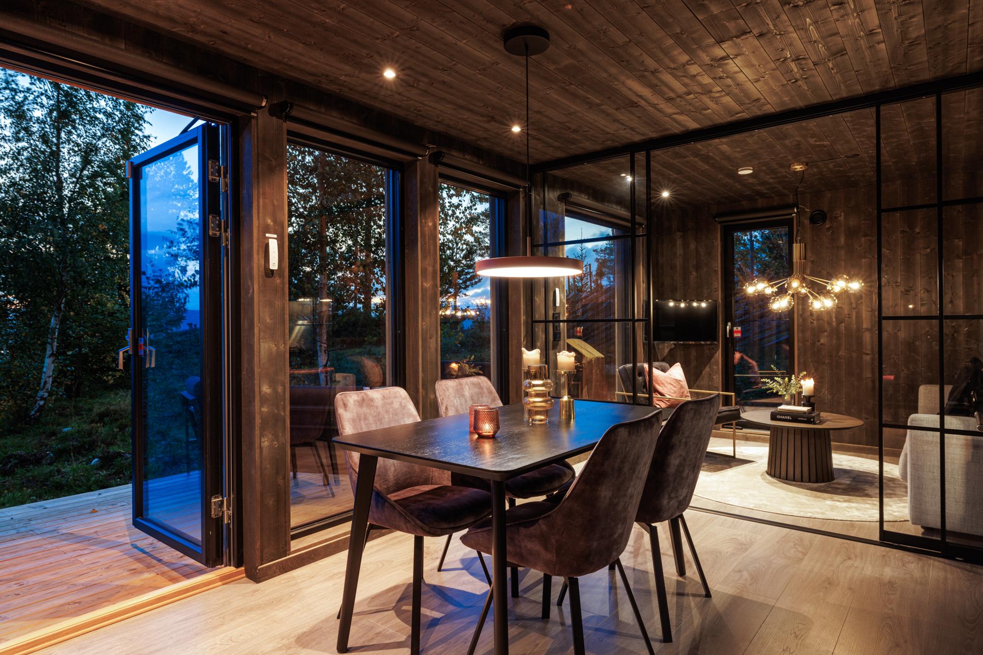 Moderne spisestue med store glassdører, mørke vegger og utsikt mot naturen.