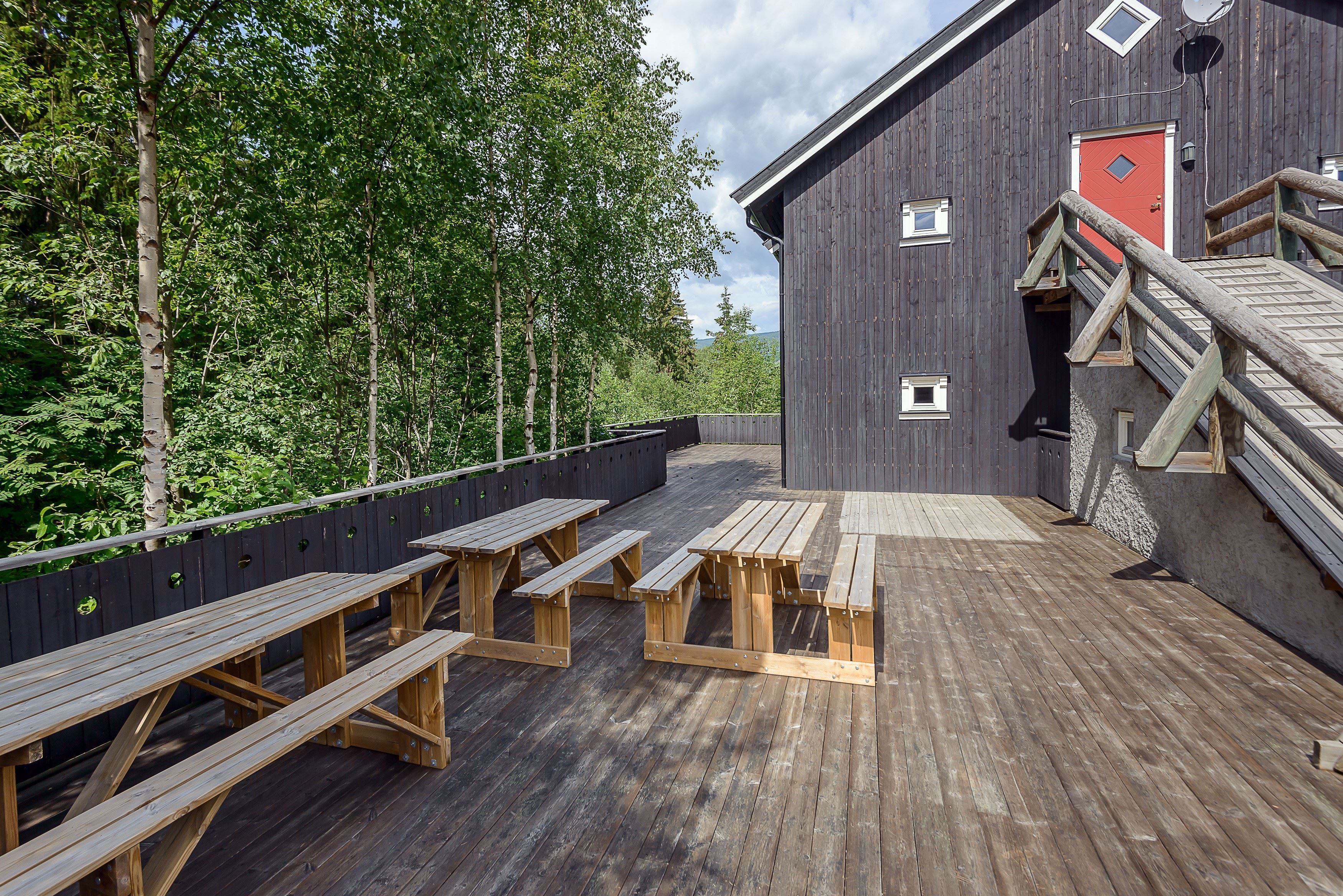A wooden terrace with benches and a building in the background.