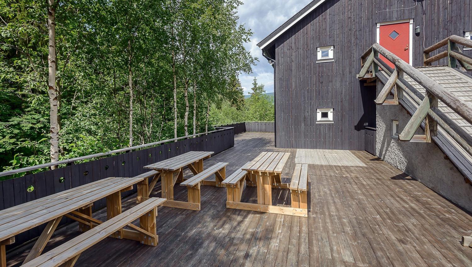 A wooden terrace with benches and a building in the background.
