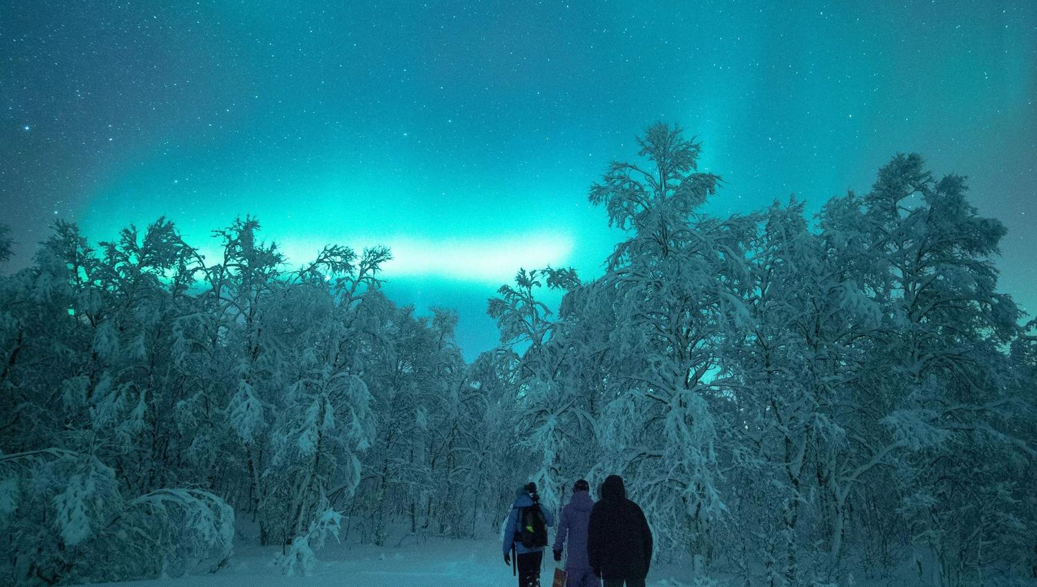 winter landscape, three people on a snowshoe trip, with a glowing sky with northern lights