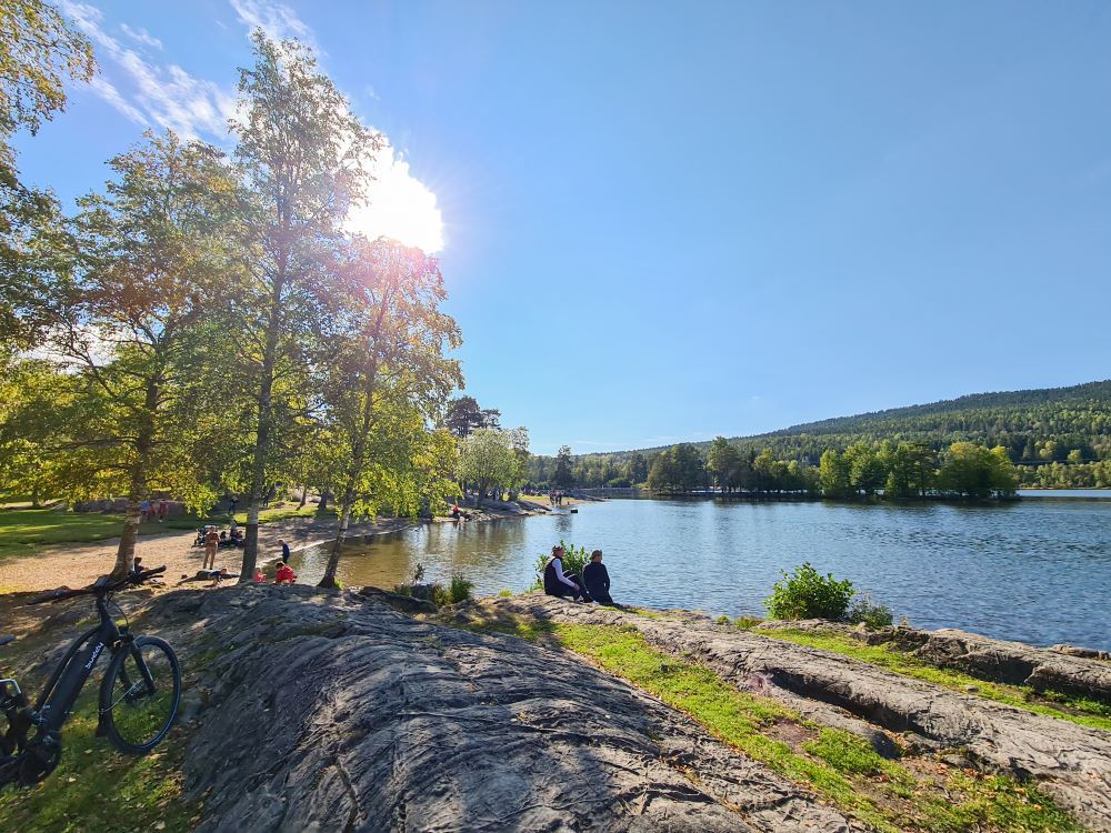 Stranden ved Sognsvann med personer som sitter ved vannet