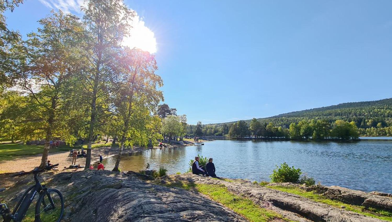 Stranden ved Sognsvann med personer som sitter ved vannet
