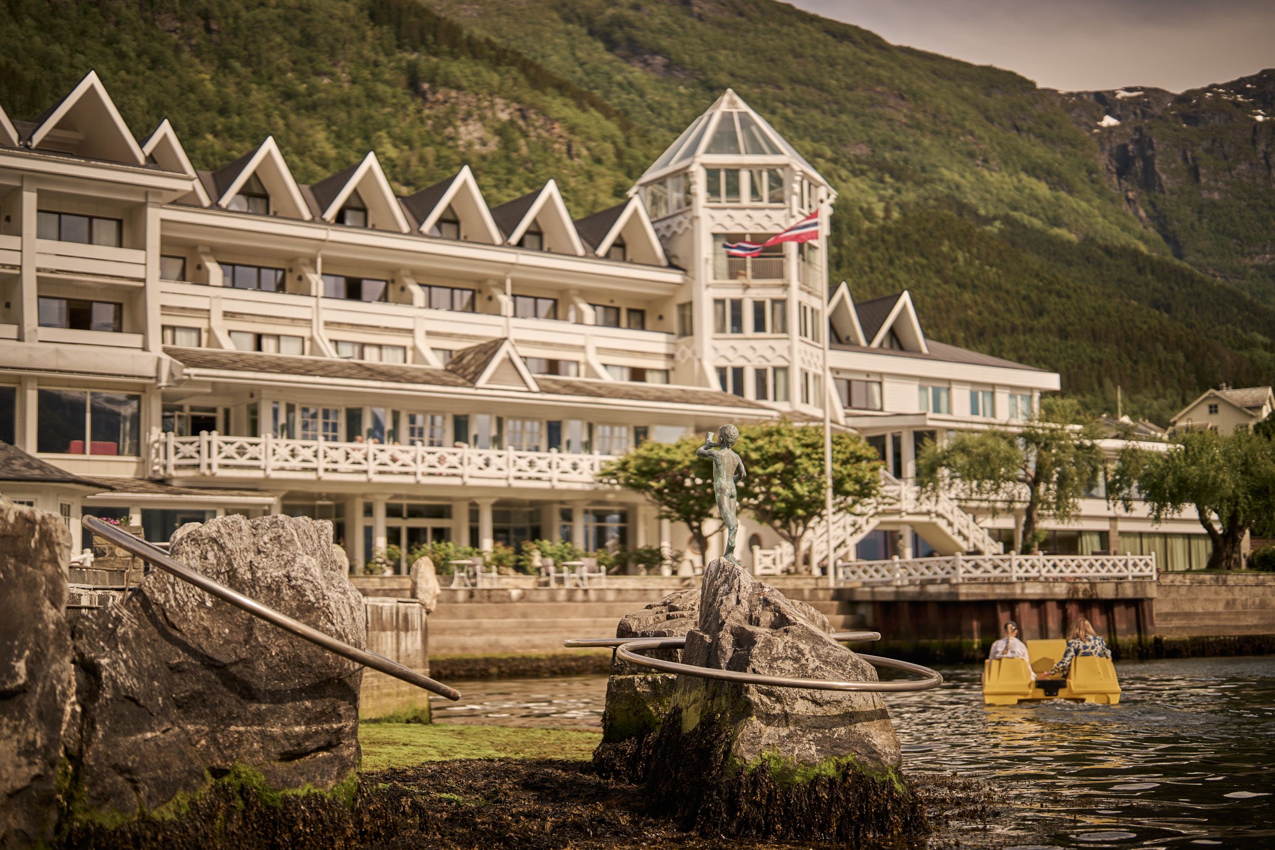 Gjestene kosar seg i pedalbåt med Hotel Ullensvang og fjella i bakgrunnen.