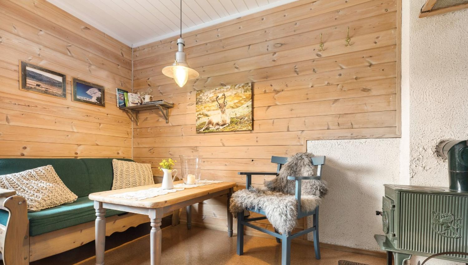 Rom med trevegger, grønn sofa og en vedovn.