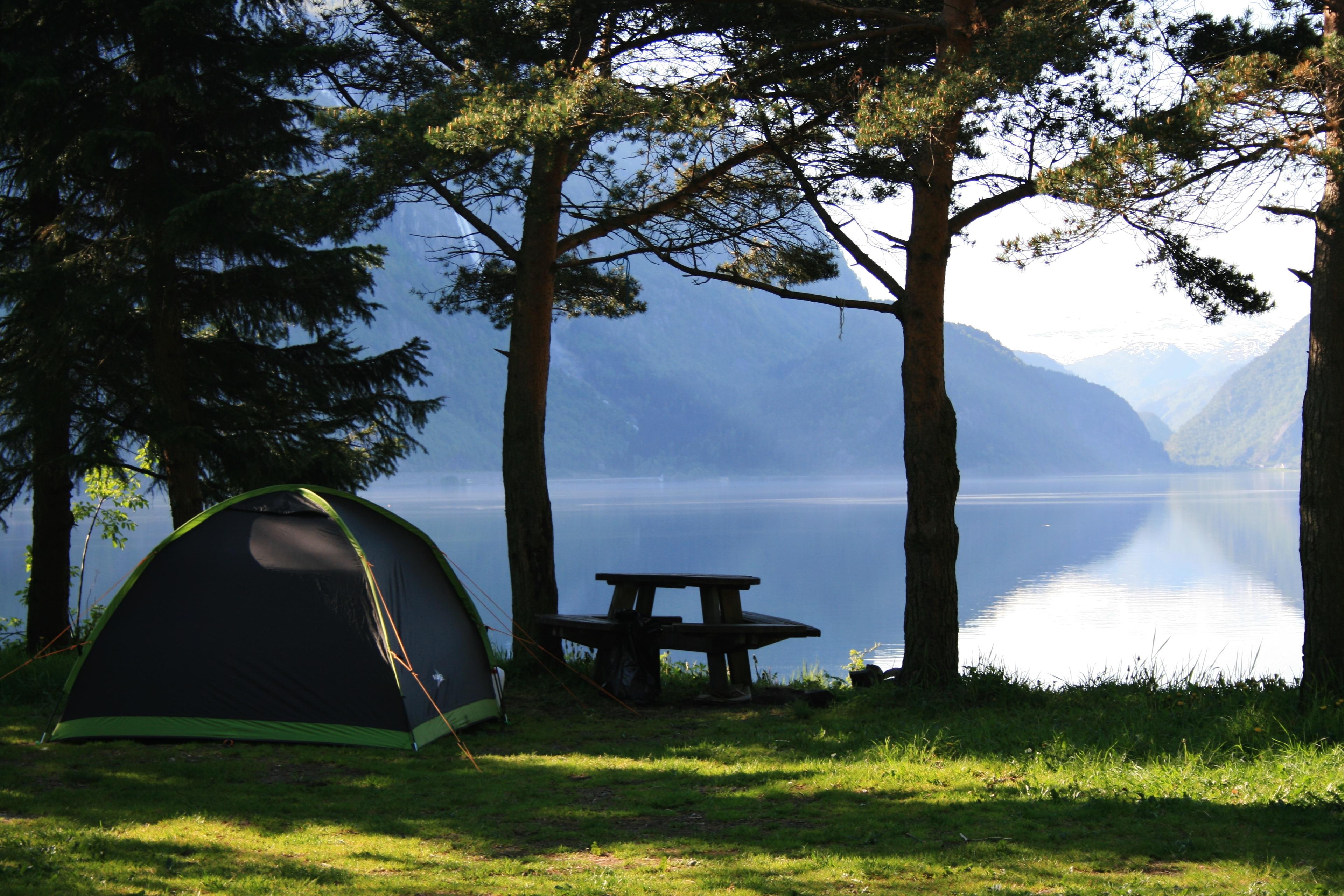 Tent pitch by the fjord with calm water and mountain views.