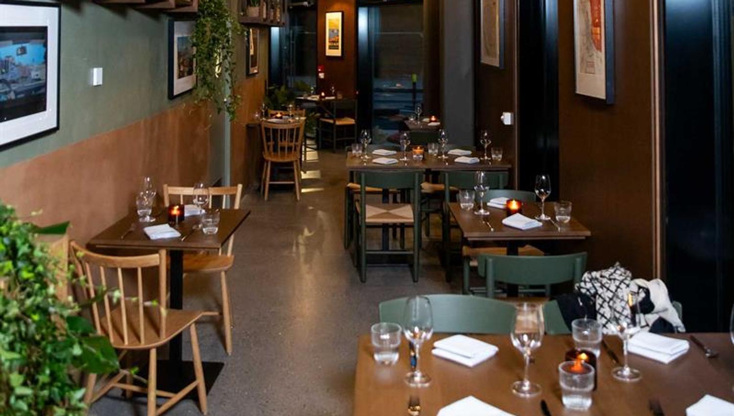 Restaurantinteriør med stor takhøyde, små dekkede trebord og stoler