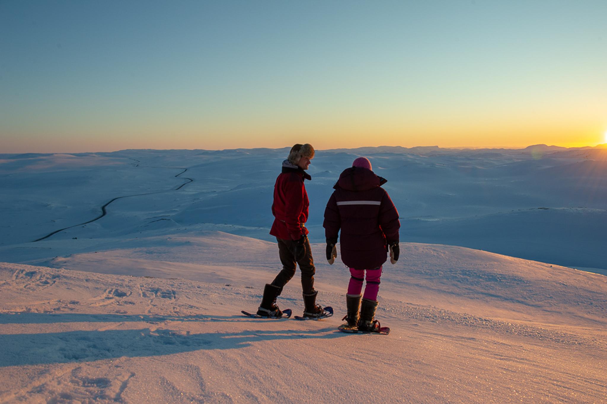 To personer på truger på toppen av Halnekollen i vinterlandskap i solnedgang.