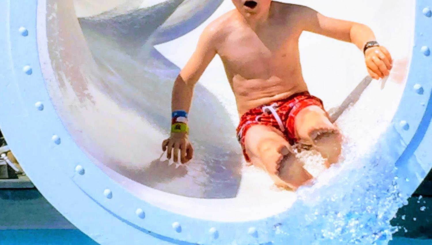 Child sliding down a water slide in the pool area at Mikkelparken