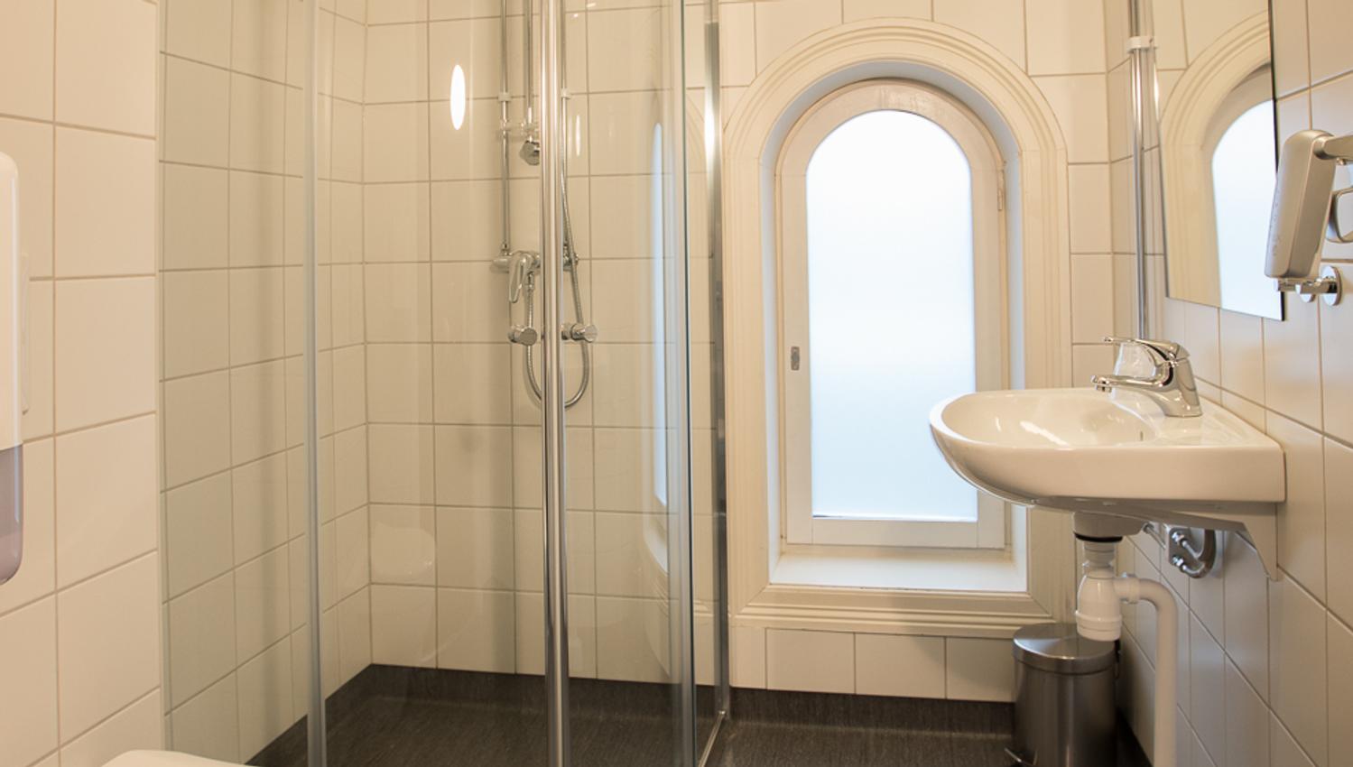 Bad med dusj. Hvite fliser, mørkt gulv. Saga Hotel & Poshtel Oslo Central. Foto