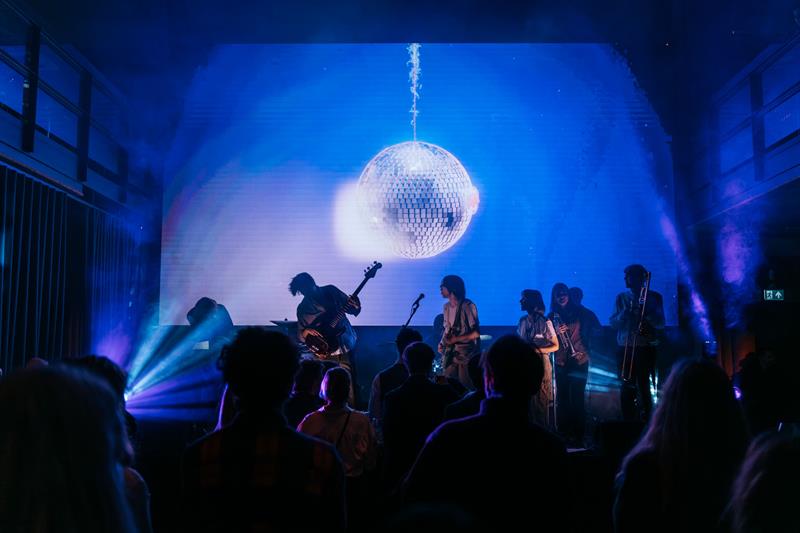 Band som spiller konsert foran publikum, under en stor diskokule