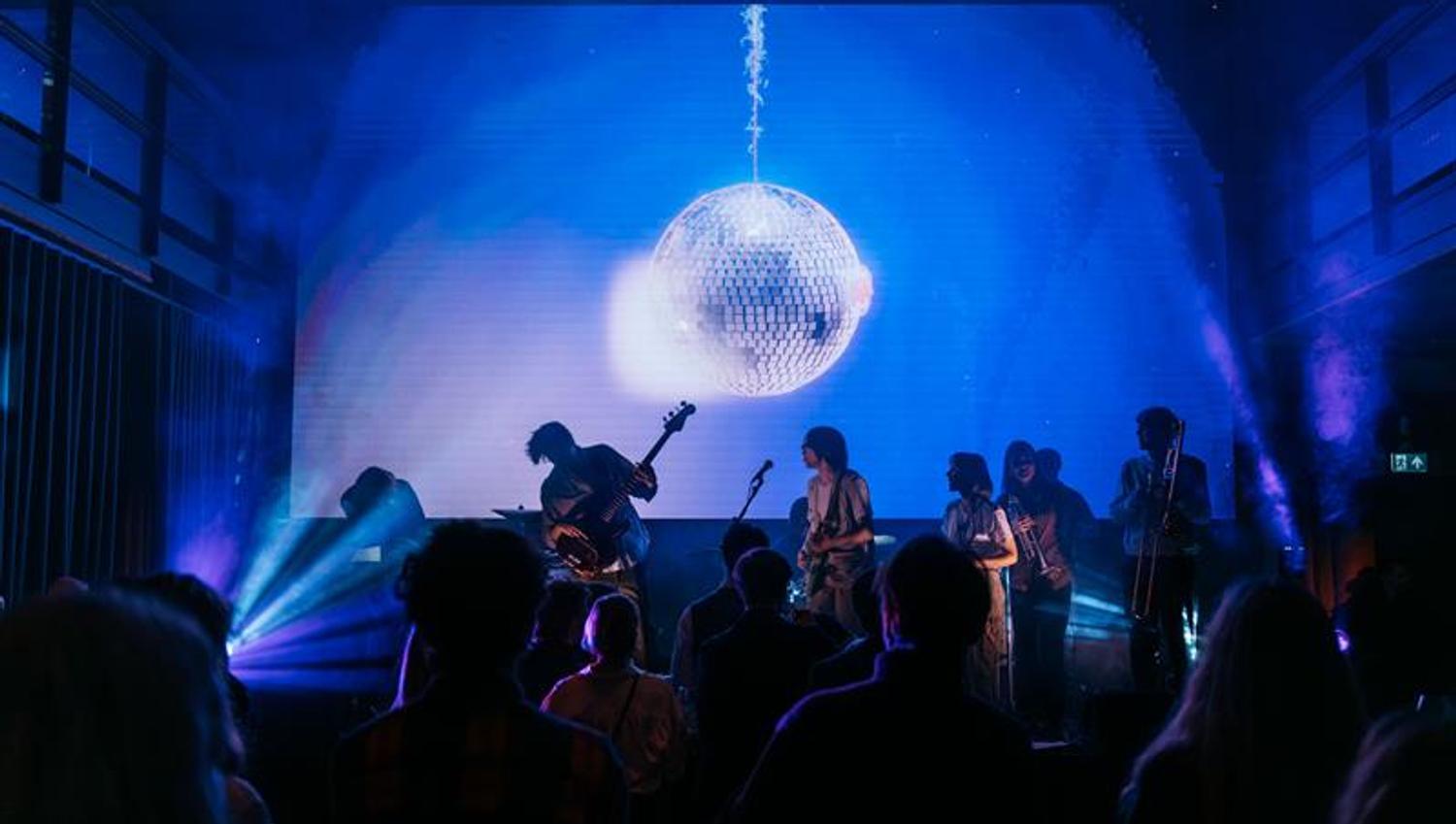 Band som spiller konsert foran publikum, under en stor diskokule
