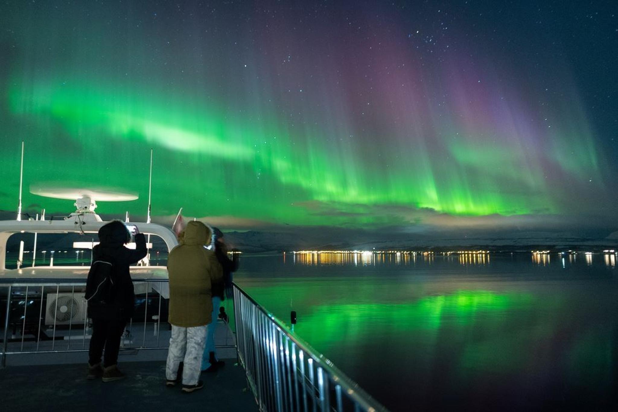 Two people taking photos of the Northern Lights from the boat's deck