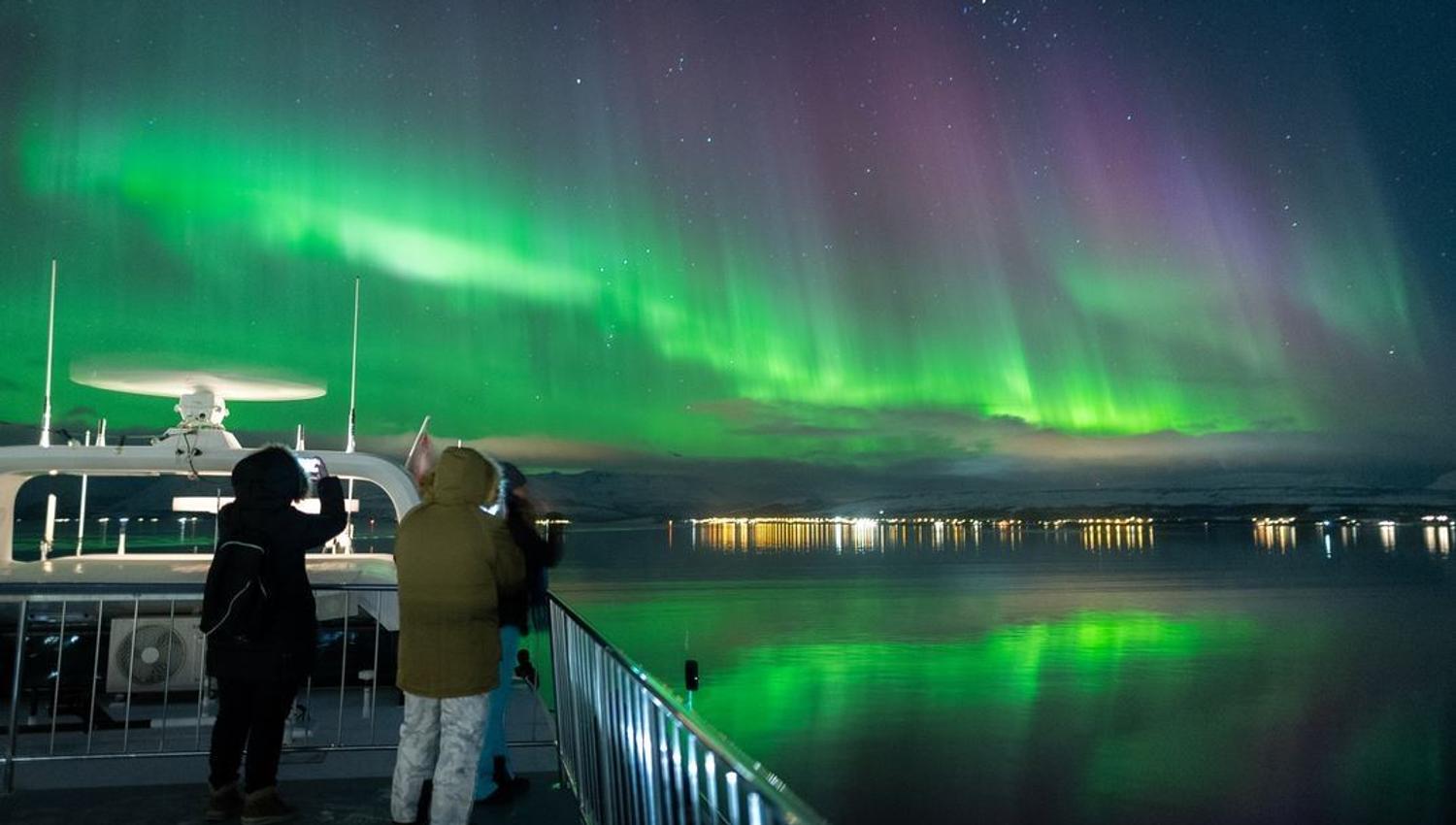 Two people taking photos of the Northern Lights from the boat's deck