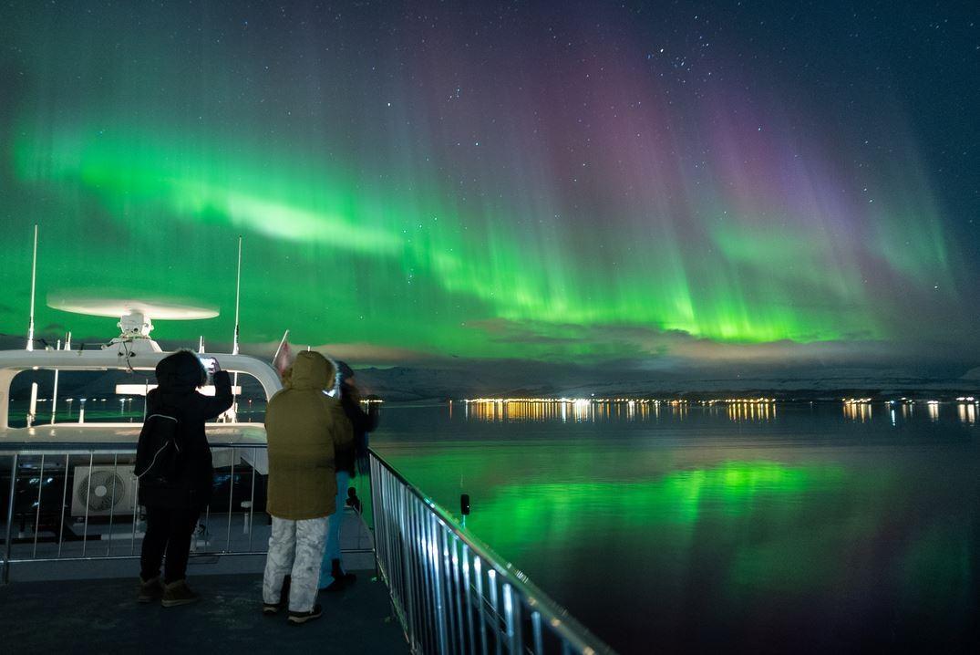 Two people taking photos of the Northern Lights from the boat's deck