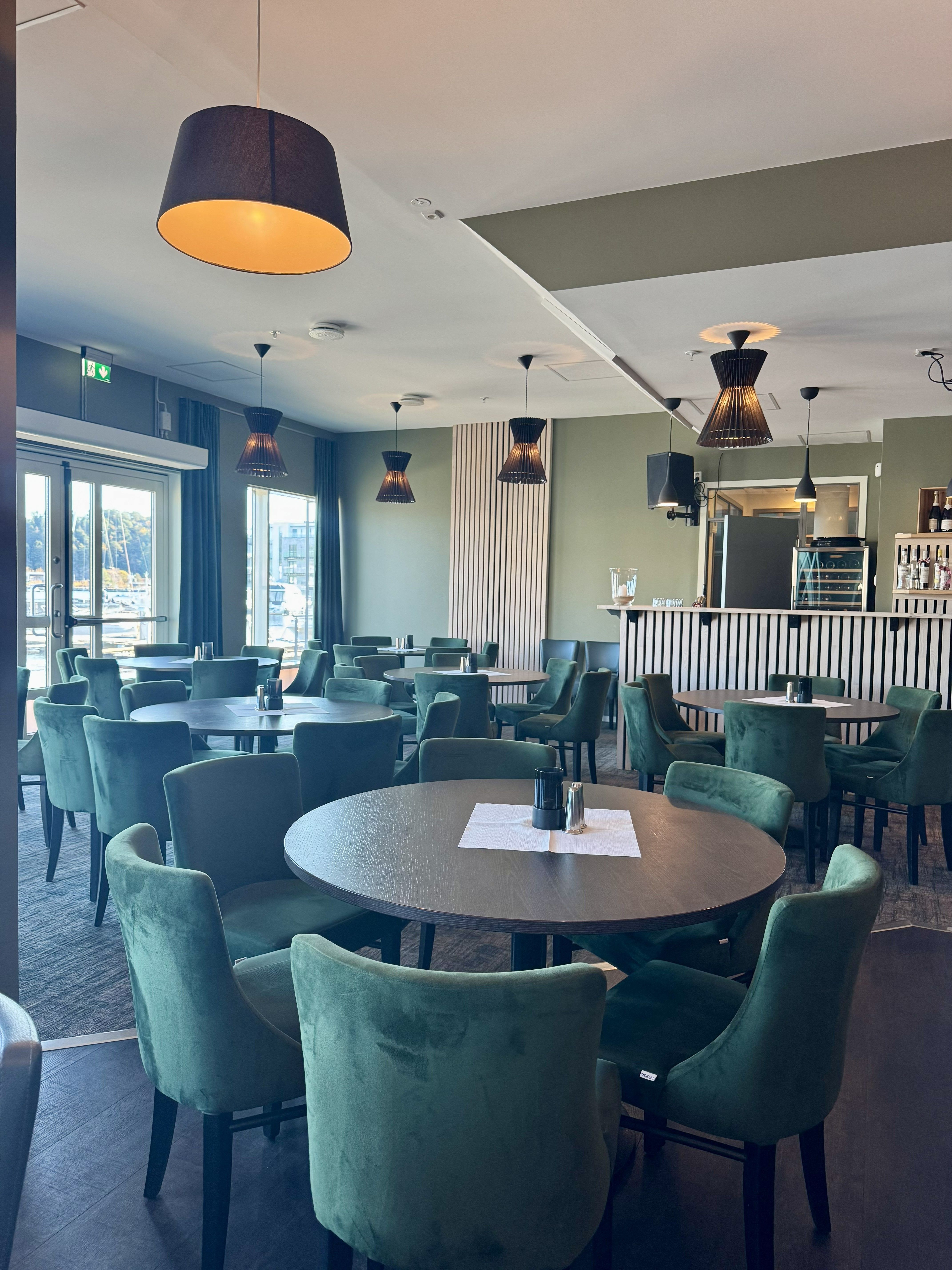 Dining hall with green chairs and round brown tables, featuring slatted details on the walls.