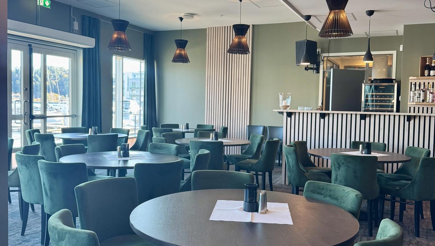 Dining hall with green chairs and round brown tables, featuring slatted details on the walls.