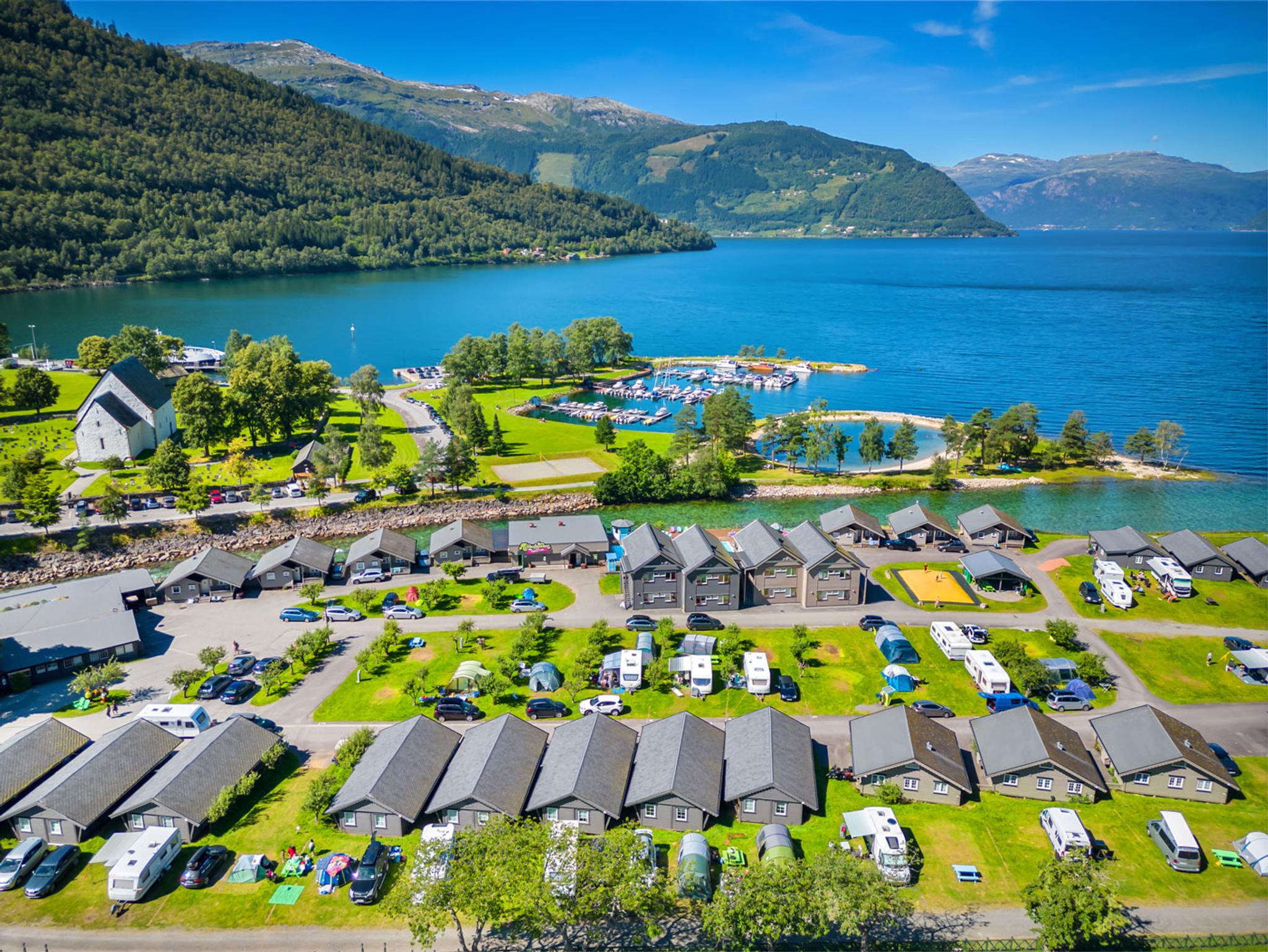Aerial view of Mikkelparken Ferietun in Kinsarvik, surrounded by the Hardangerfjord and stunning mountains. A perfect holiday destination for the whol