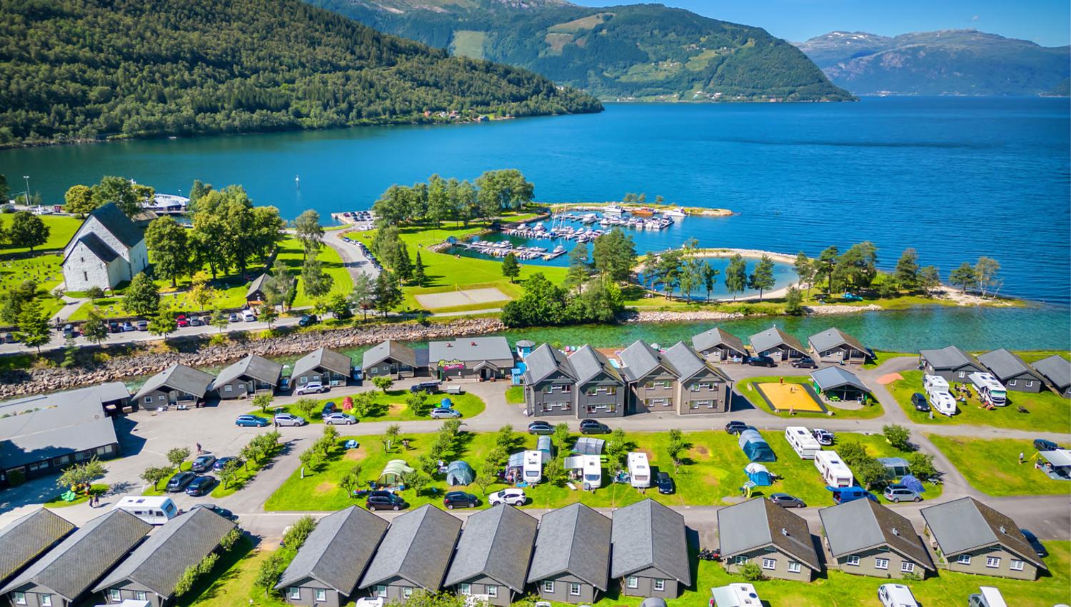 Luftfoto av Mikkelparken Ferietun i Kinsarvik, omgitt av Hardangerfjorden og majestetiske fjell. Perfekt feriestad for heile familien.