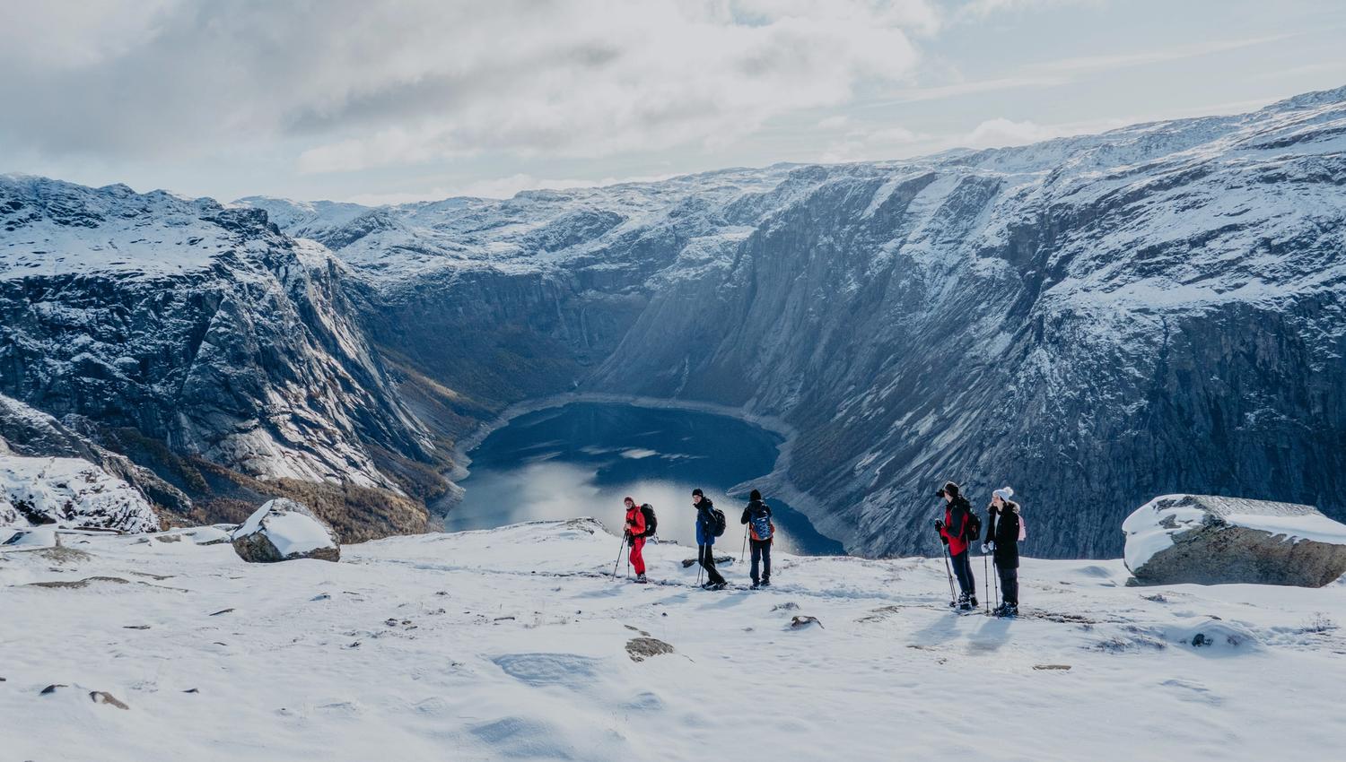 Group snowshoe hiking near Trolltunga with a view of the fjord and snow-covered mountains.