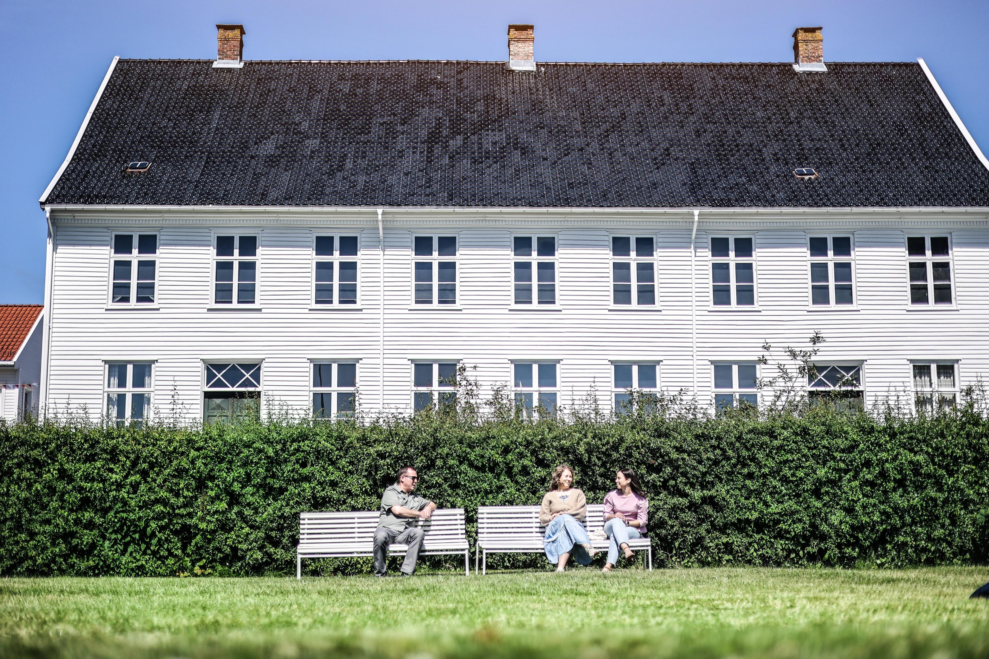 Two white benches in front of the museum with three people.