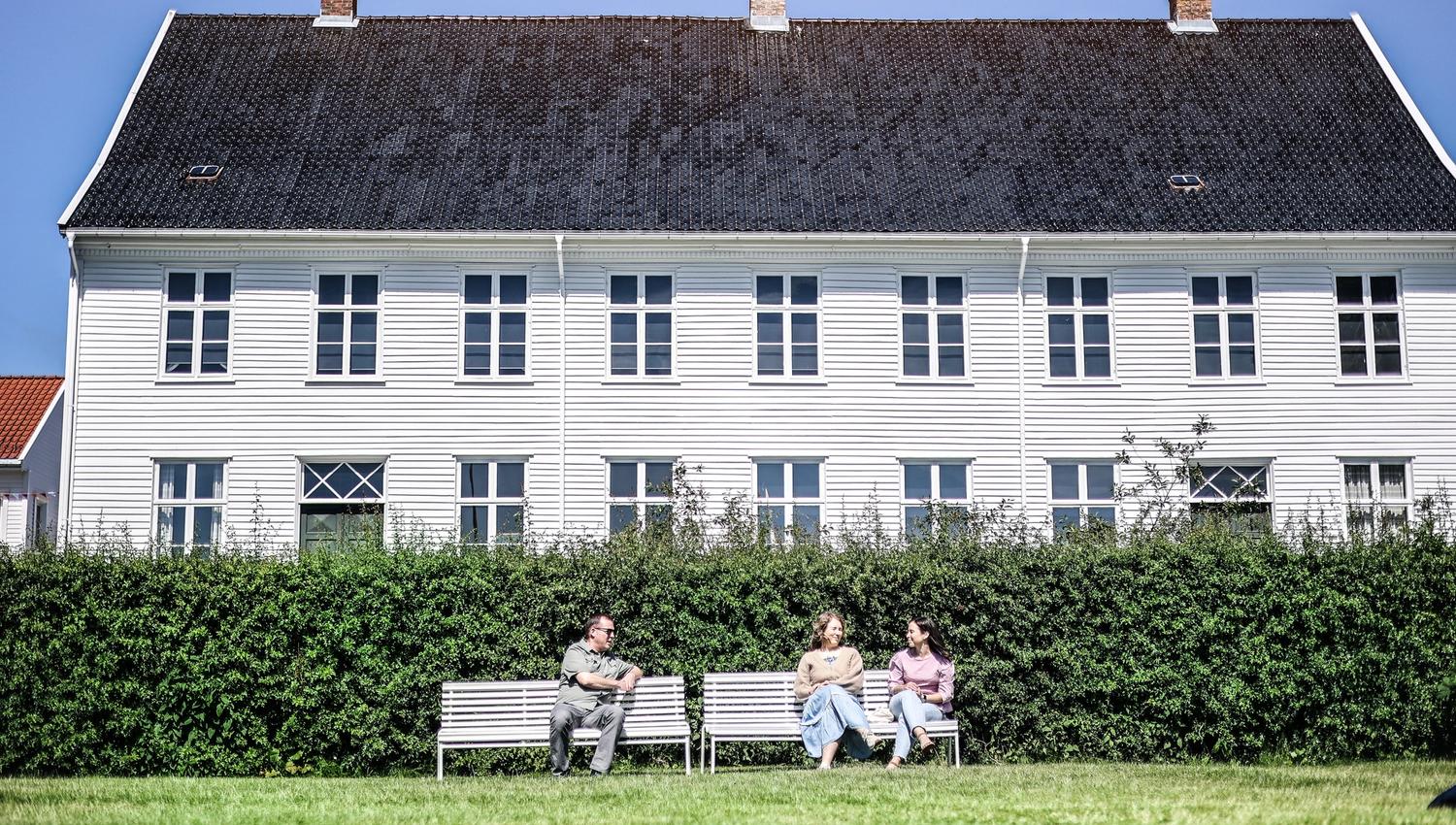 To hvite benker foran museet med 3 menneskerr.