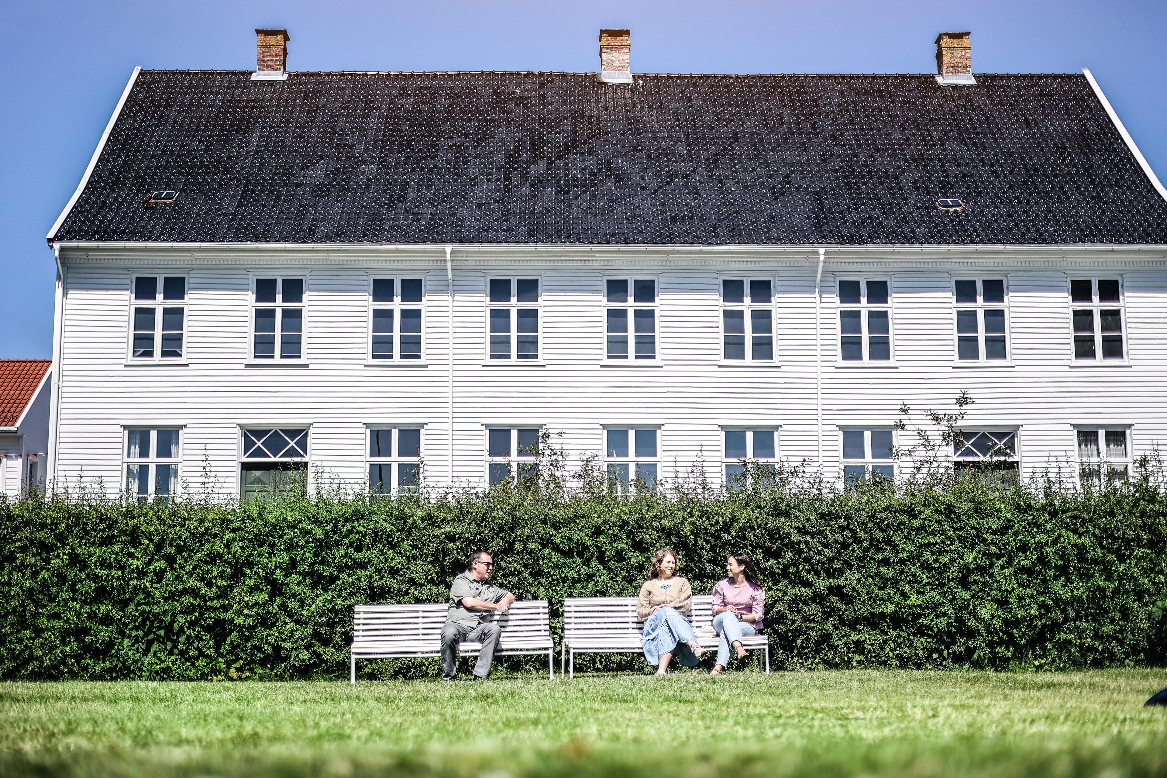 Two white benches in front of the museum with three people.