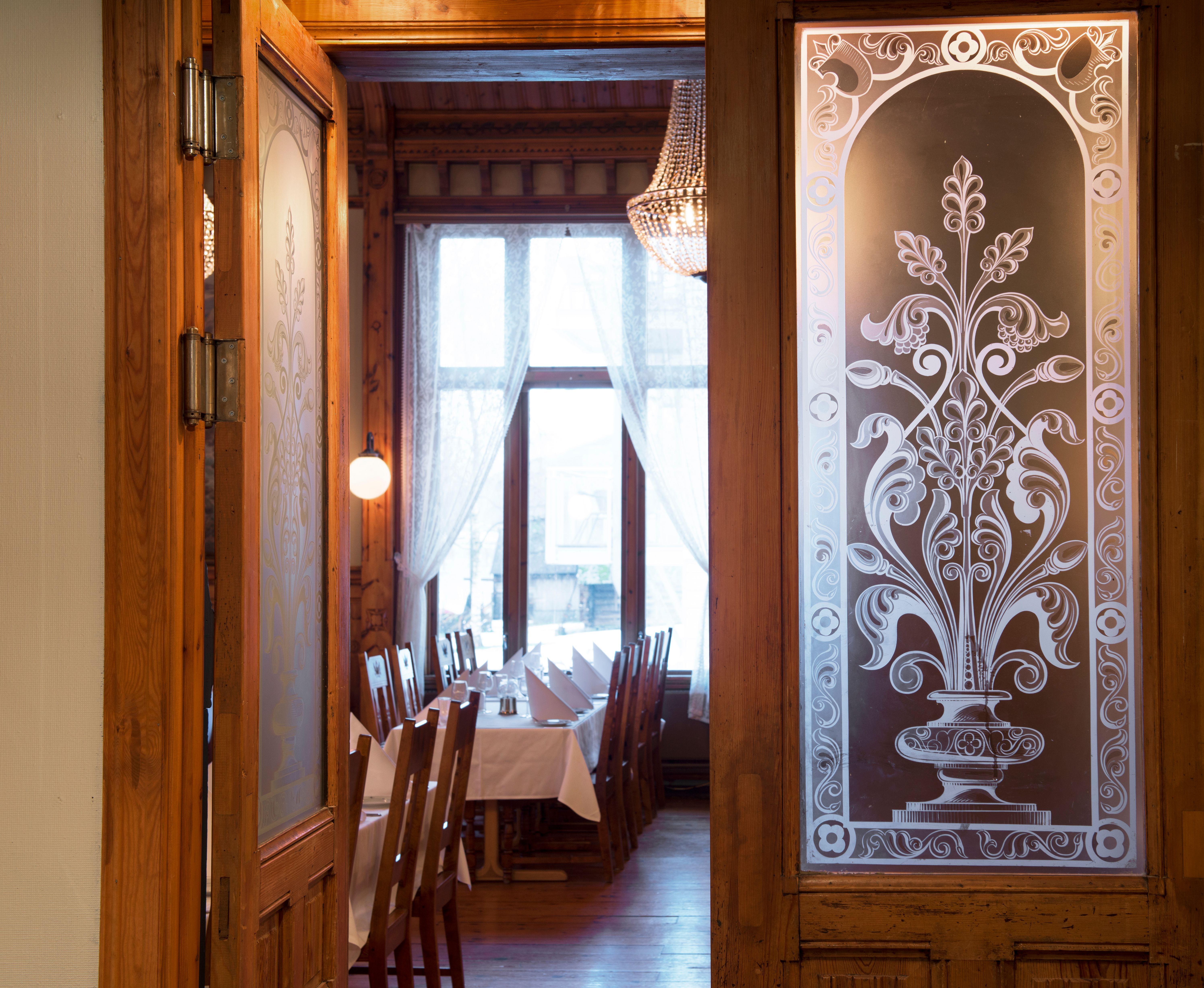 Stemningsfull inngang til restauranten på Thon Hotel Sandven, med klassiske utskjeringar og glasdetaljar.