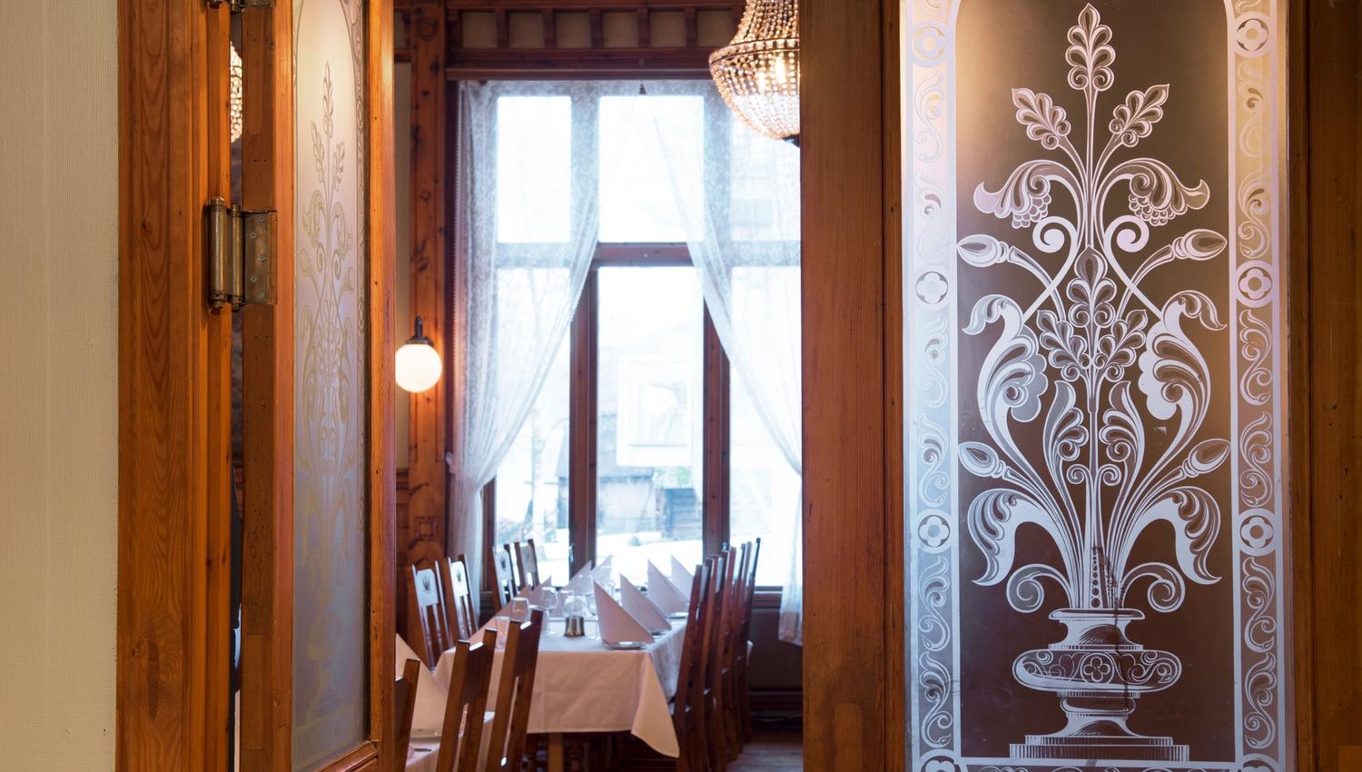 Stemningsfull inngang til restauranten på Thon Hotel Sandven, med klassiske utskjeringar og glasdetaljar.