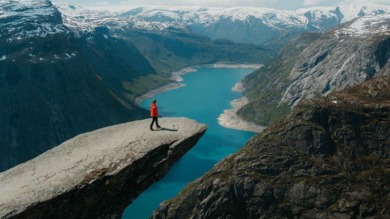 A hiker stands at the edge of Trolltunga overlooking Lake Ringedalsvatnet and the dramatic mountain landscape in Hardanger.
