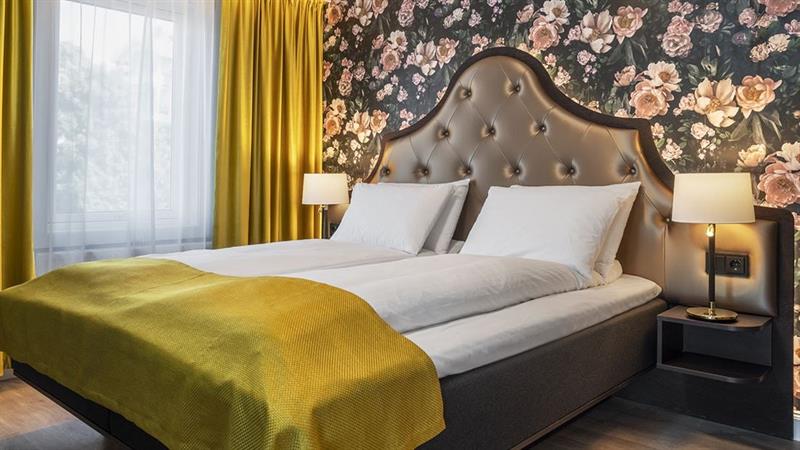 Soverom Thon Hotel Høyers. Seng med gult teppe, blomstrete tapet på vegg.