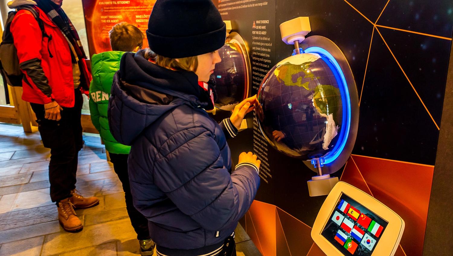 A boy playing with one of the interactive exhibition items, a globe in the wall.
