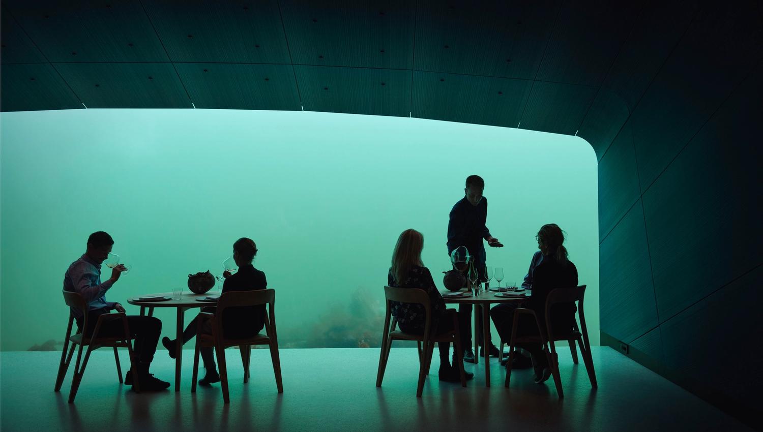 Two couples at separate tables, a waiter serving one of the tables. View toward the water, but mostly greenery and little to see.