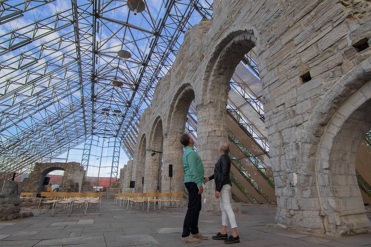 Interior view of the Hamardomen protective structure, showing tall glass walls and wooden beams surrounding the cathedral ruins. The natural light giv