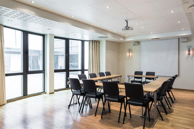 lyst møterom med langbord, stoler og store vinduer som slipper inn dagslys.