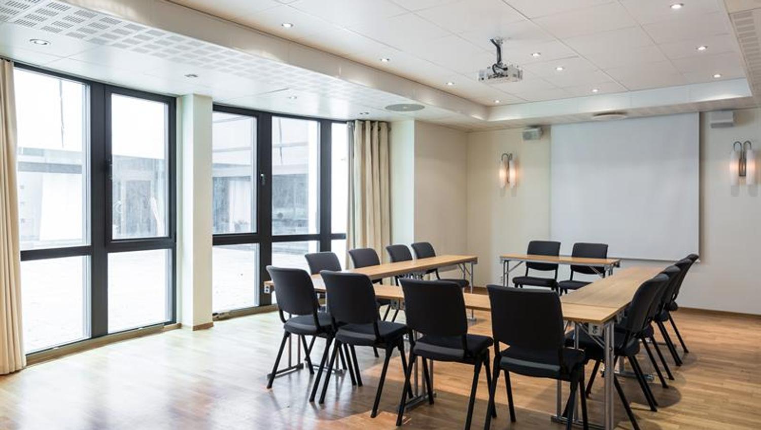 lyst møterom med langbord, stoler og store vinduer som slipper inn dagslys.