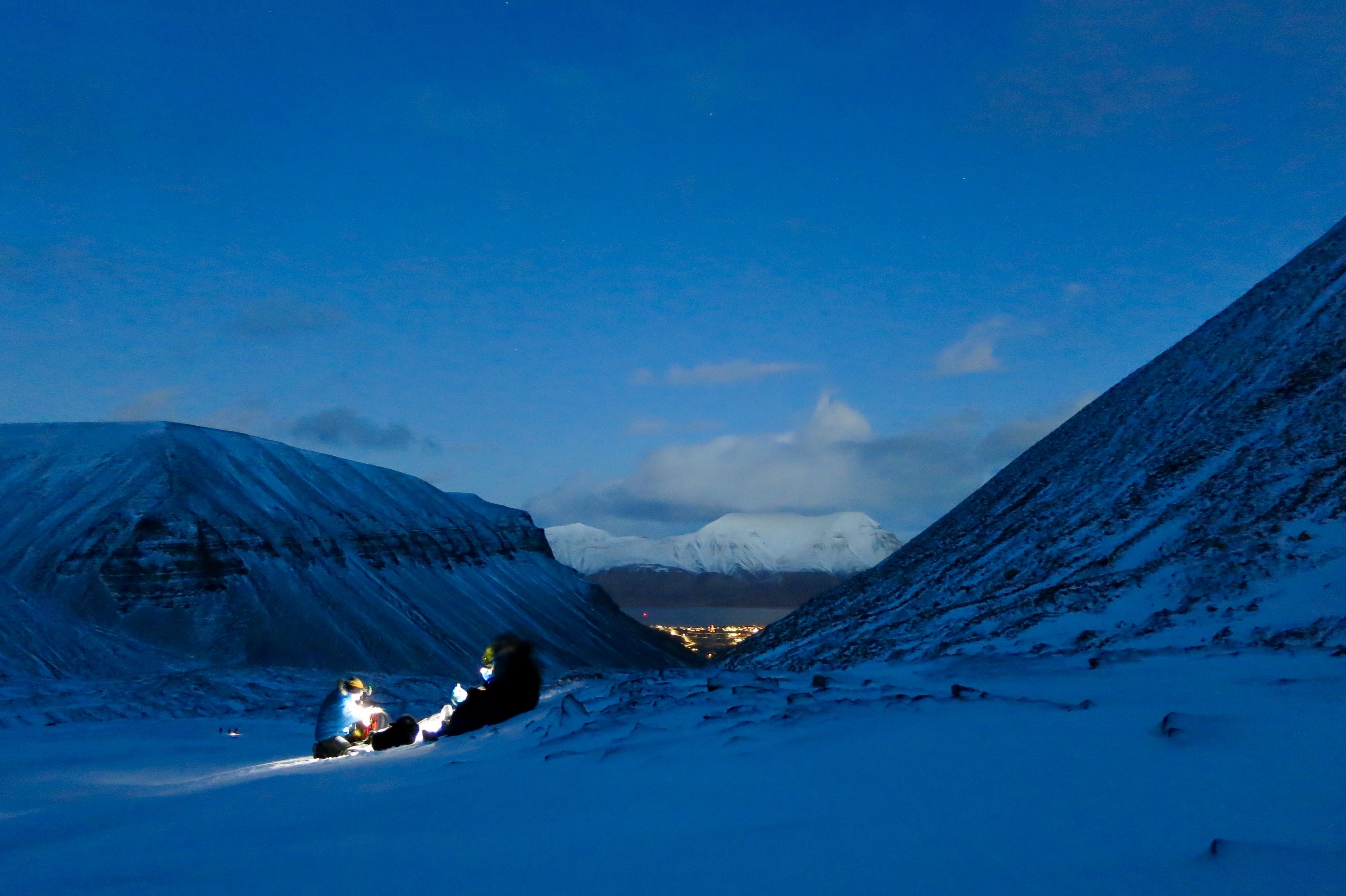Two people with headlamps in the foreground, with mountains and Longyearbyen in the background.