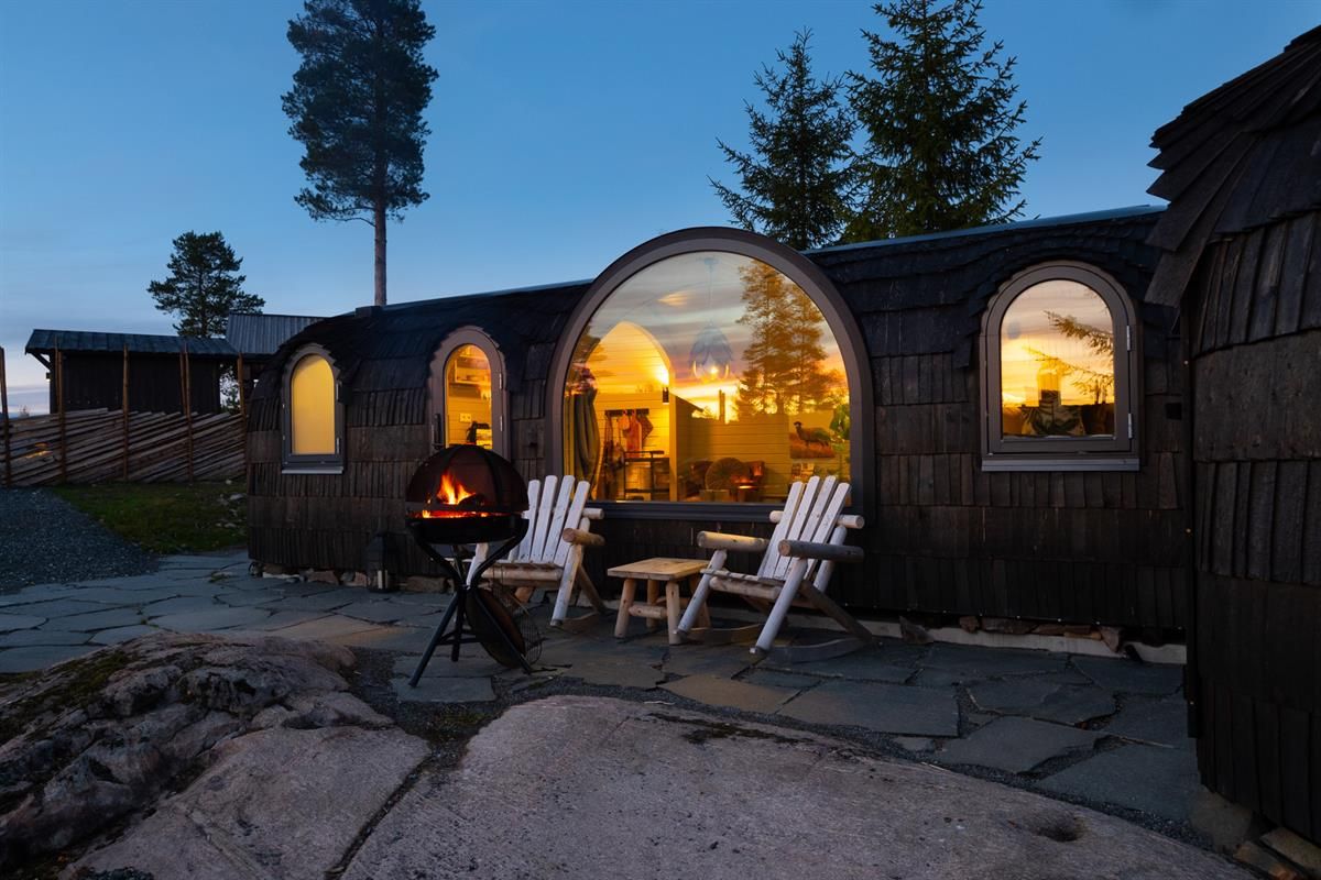  Oval wooden cabin pods with large windows and an outdoor seating area at dusk.
